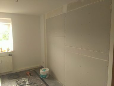 Leere Innenraumwand mit frischem Putz und einer Fenstersicht.